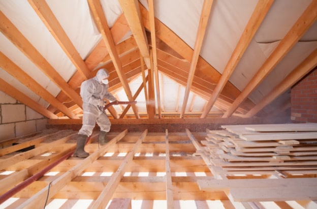 Person in Hazmat suit in attic applying blow-in insulation